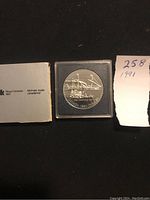 1991 Canadian silver dollar coin in plastic case with original Royal Canadian Mint box and documentation visible.