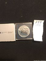 Front view of 1992 Canadian silver dollar coin in plastic case, showing horse-drawn sleigh detail and inscription.