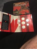 Overview of closed folder with the coins visible inside mounted in their slots and the outer folded cover with 'Oh Canada!' title and maple leaf design.