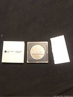 Silver dollar coin in plastic case with Royal Canadian Mint packaging on black background.