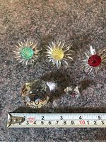 Top-down view of the seven crystal items arranged on a countertop with measuring tape; three crystal flowers with green, yellow, and red centers; large faceted crystal paperweight; small teddy bear; small dragonfly and pendant crystals.