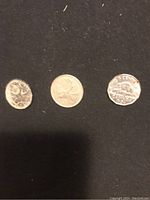 Three loose Canadian coins on black background: the 1943 quarter, 1968 quarter showing caribou design, and 1954 nickel showing beaver design.