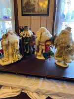 Photo showing all five standing Santa figurines in varying cream, red, and gold colors arranged together on a flat surface