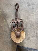 Top-front view of antique metal pulley with wooden wheel and strong metal loop.