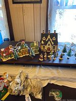 View of the entire Christmas town set showing 4 ceramic houses with lights, 10 ceramic people figures, and 5 small artificial trees arranged on a black surface