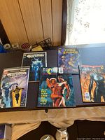 Lot of five comic books arranged on table against wood panel background. Includes two Superman comics, Marvel Swimsuit Special, and two Tomb Raider comics.