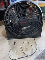 Front view of Honeywell black floor fan showing grille and Honeywell logo.