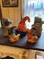 Front view of two ghost tree stump decorations, dancing witch hat, and two Halloween ceramic tabletop lanterns.