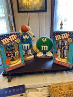 Two M&M candy dispensers with two boxed Millennium Time Capsules displayed on a table indoors.