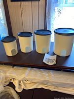 Four white canisters with black lids displayed on table, showing clear windows near the bottom.