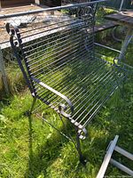 Black bent metal outdoor love seat bench photographed outdoors on a grassy surface.