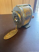 Front angled view showing the pencil insertion side, metal body, and attached golden tag with branding.