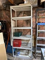 Full view of tall beige plastic shelving unit in garage with items on shelves for scale.