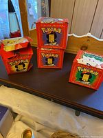 Four red Pokémon limited edition boxes for 23K gold plated trading cards and one opened box with spherical black protective case containing a gold plated card.