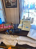 Relsew serger sewing machine setup on dark surface next to a box with multiple spools of thread in assorted colors and power cord.