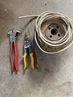 Photo showing two cutting tools with red and yellow handles next to a metal spool wound with white wire.