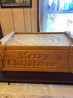 Front view of rectangular wooden box with carved 'Merry Christmas' text and Santa Claus face.