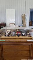 Front view of wood and acrylic display case with five die cast cars including cream, black, and red cars visible inside, some parts detached.