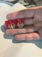 Close-up photo of the pair of gold butterfly earrings held in hand showing detailed filigree design and hooks.