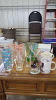 Table surface with seven highball glasses, four mugs, and additional glassware grouped together
