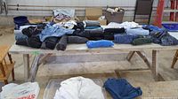 Overview of various men's clothing items including folded shirts of different colors and styles on a wooden table in a workshop setting.