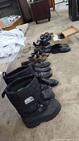 Line of men's boots, dress shoes, sandals on floor showing condition and variety