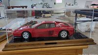 Side view of red Ferrari Testarossa model in plexiglass display case on wooden base