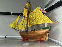 Wooden model sailboat with yellow fabric sails on red display stand, showing right side profile and rigging detail.