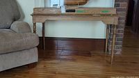 Full view of the entire wooden hall sofa table next to a couch and brick fireplace, showing top surface and legs.