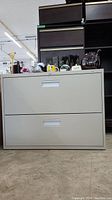 Front view of a beige two-drawer filing cabinet with integrated handles and no visible decals except a Staples logo.