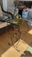 Side angle of small metal table showing tile top and curved metal legs with flower design.