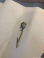 Close-up image of 18k gold tie tack showing engraved square face and chain with bar.