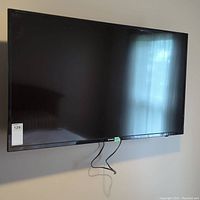 Front view of the black Skyworth 50" flat screen TV mounted on wall with visible cables hanging down.