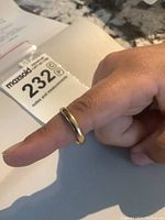 Domed yellow gold band on finger with MaxSold lot card in background