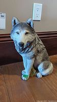 Full frontal view of hand painted Sandicast wolf sculpture showing detailed fur texture, yellow eyes, and green marking on one front paw.