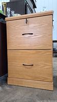 Front view of the wood filing cabinet showing two drawers with black metal handles and key locking the top drawer.