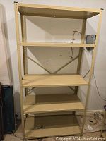 Photo of one gold-colored metal utility shelving unit with five shelves against a wall