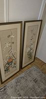 Two framed vintage Chinese paintings standing side by side on floor, showing overall view of lot