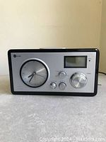 Front view of vintage Camden tabletop AM/FM radio alarm clock showing analog clock face on left, digital display on right, and control knobs below.