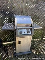 Full view of the Coleman propane BBQ grill showing metal body, side shelves and base storage compartment