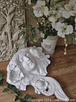 Figural wall font, female face sculpture, wall plaque, and plant vase grouped on wood surface