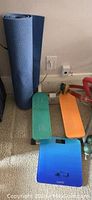 Blue yoga mat rolled up beside a two-step stepper with orange and green pedals on a blue base