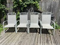 Front view of four greige powder-coated aluminum patio chairs aligned on wooden deck with scrollwork details.