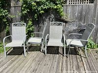 Full front view of four patio chairs arranged side by side on a wooden deck with greenery in background.