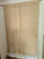 Full view of the tan jute and cotton handwoven wall hanging with tassel and geometric diamond pattern hung from wooden rod.