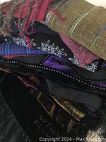 Pile of assorted scarves and stoles including woven, ikat, velvet and embroidered textiles in varied colors and patterns.