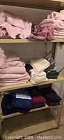 Several shelves with stacks of towels organized by color including pink, cream, navy, burgundy, and blue. Towels folded neatly and piled in multiple stacks.