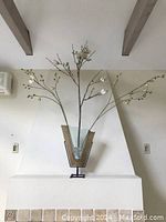 Front view of the vase with faux branch arrangement placed on a white mantel against a light-colored wall, showing the full height and detail of the three branches.