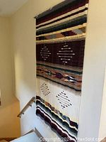 The very large vintage Southwestern wool wall hanging displayed vertically on a stair wall, showing full length and colors.
