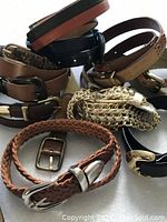 Photo showing a pile of belts including brown braided leather, chain-link style, and smooth leather belts primarily in neutral tones